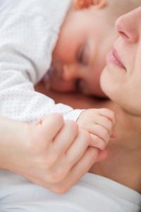 Peaceful woman lying with her baby who is sucking a pacifier ind